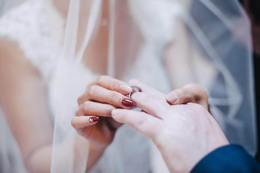 A bride is putting her wedding ring on the bride's finger.