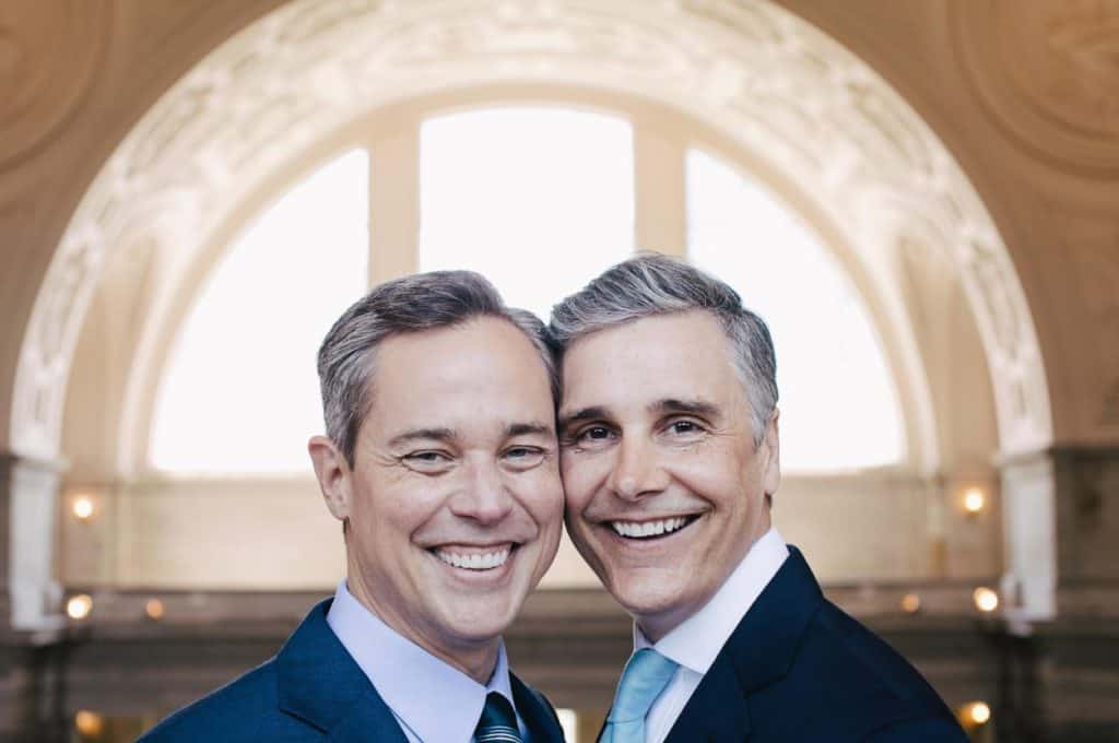 Two men in suits smiling in front of an arch.