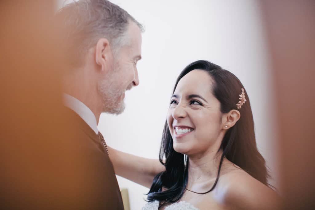 A bride and groom smiling at each other in front of a mirror.