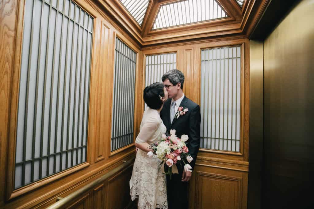 A bride and groom kissing in an elevator.
