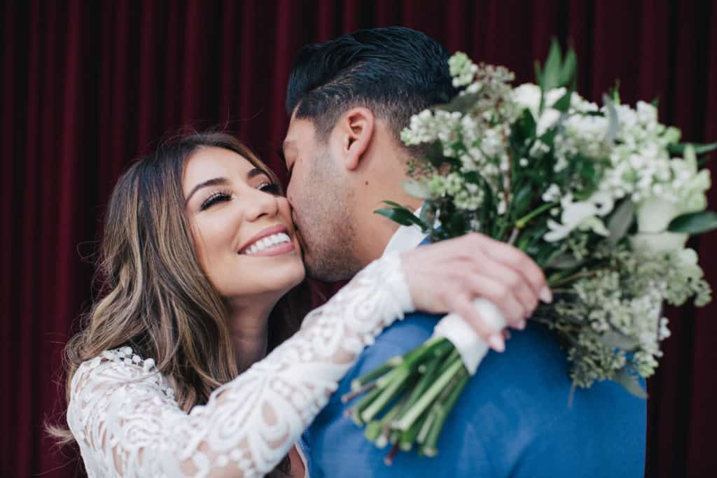 A bride and groom kissing in front of a curtain.