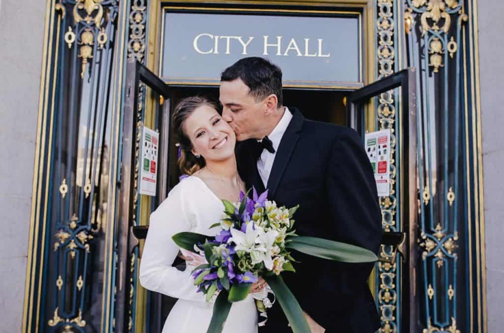 A bride and groom kiss in front of the city hall.