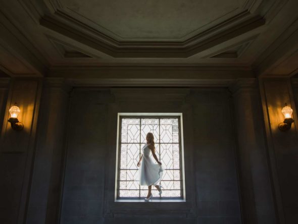 A woman in a white dress standing in front of a window.